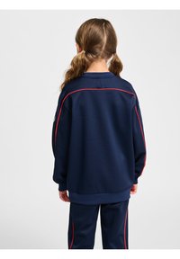 Mörkblå sweatshirt med röd accentpiping, med rund hals och långa ärmar, tillverkad av ett mjukt tyg. Styld med matchande byxor.