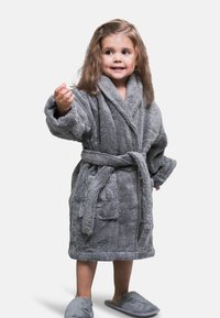 Accappatoio grigio in peluche con cintura, due tasche frontali e finitura testurizzata. Pantofole grigie coordinate completano l'outfit. Il bambino sorride e posa.