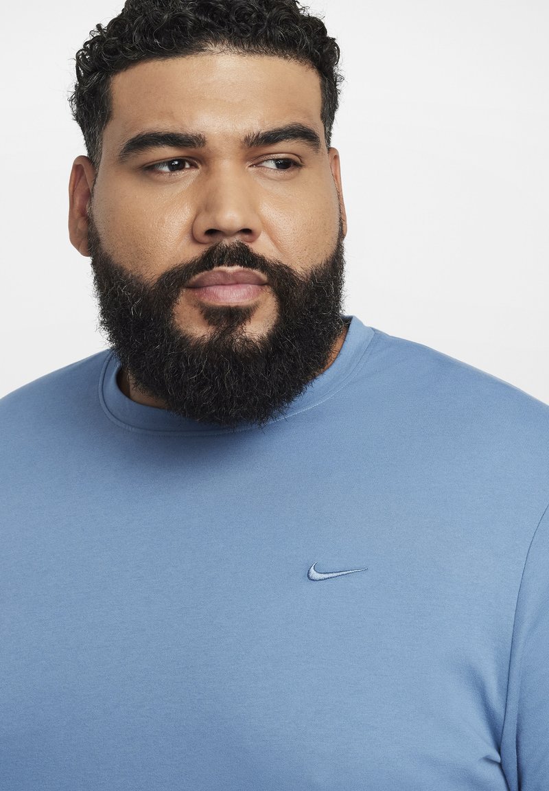 Jasnoniebieska bawełniana koszulka z okrągłym dekoltem i krótkimi rękawami. Posiada małe, haftowane logo Nike po lewej stronie na klatce piersiowej. Gładka tekstura.