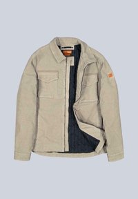 Hellbeige gesteppte Jacke mit zwei Brusttaschen, schwarzem Innenfutter, Druckknopfverschluss und oranger Etiketten-Detail am Ärmel.