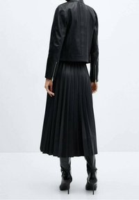 Veste en cuir noire au design court, associée à une jupe plissée noire. Des bottes noires à talons hauts complètent la tenue.