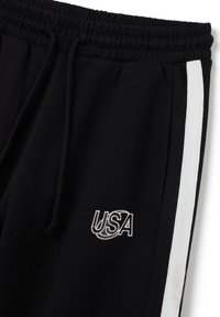 Pantalones de chándal negros con una franja blanca a lo largo del costado, cinturilla elástica, cordón y logo bordado "USA" en la parte delantera.