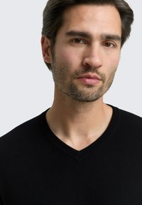 Schwarzer V-Ausschnitt-Pullover mit strukturiertem Strick, geripptem Ausschnitt und schmaler Passform, vor einem hellgrauen Hintergrund präsentiert.