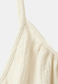 Gros plan sur un tissu de couleur crème avec un design texturé et froncé, doté d'une bretelle étroite, montrant les coutures et les détails du matériau doux.