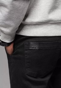 Czarne dżinsy z denimu z skórzaną metką na tylniej kieszeni, w połączeniu z szarym swetrem. Tkanina wydaje się miękka o gładkiej teksturze.