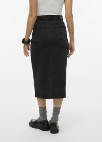 Högmidjad svart denimkjol med rak skärning, utrustad med två bakfickor och knä-långs nederkant. Bärs med grå strumpor och svarta loafers.