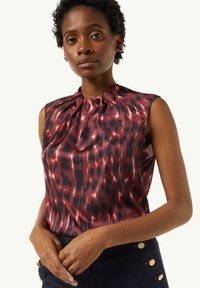 Bezramiona bluzka w kolorze burgundowym z czarnym wzorem zwierzęcym, z plisowanym dekoltem i gładką fakturą, zestawiona z ciemnym dżinsem.