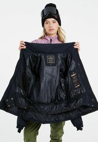 Marineblauwe skijas met een gladde voering, ritsluiting en meerdere zakken. Metalen accenten nabij de zoom en een zichtbaar label aan de binnenkant.