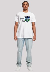 White cotton t-shirt featuring a graphic print of a blue circle with landscape, text “David Bowie The Man Who Fell to Earth” in black.