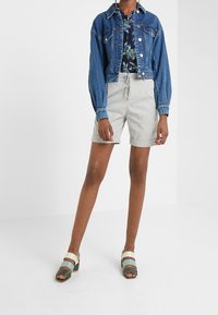 Jeansjacka, blommig skjorta, ljusgrå shorts och flerfärgade sandaler med remmar. Fokusera på material, design och färgkontraster.