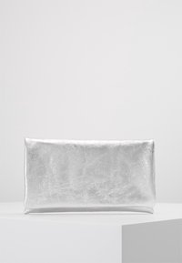 Pochette rectangulaire argentée avec une surface métallique lisse et légèrement texturée, présentée sur un socle blanc contre un fond uni.
