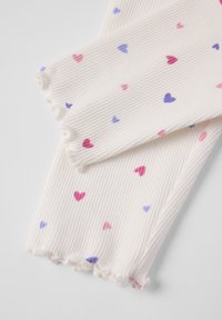 Ribbet hvid stof leggings med små lyserøde og blå hjerter. Kanterne har en frynset finish for ekstra tekstur.