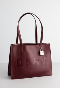 Torebka DKNY w burgundowej, pebblowanej skórze, z wytłoczonym logo, zamknięciem na zamek, podwójnymi uchwytami oraz metalowym akcentem w postaci zamka.