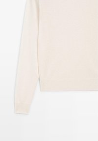 Cremefarbener Pullover mit weicher Textur, ausgestattet mit einem gerippten Saum und Bündchen. Das Design umfasst einen runden Ausschnitt und lange Ärmel.