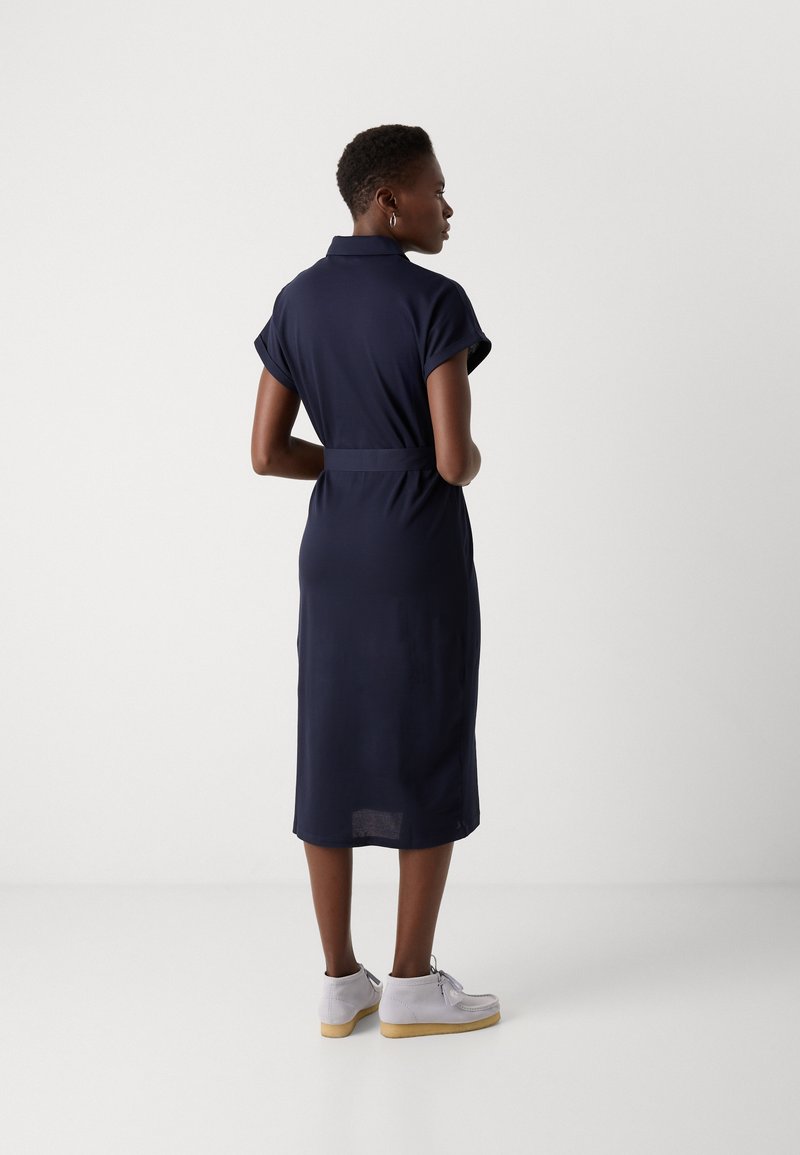 Granatowa sukienka z krótkim rękawem, z kołnierzykiem, paskiem w talii i długości midi. Wykonana z gładkiego materiału o prostym, eleganckim wzorze.