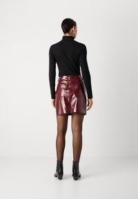 Burgunderfarbene Vinyl-Minirock mit glänzender Textur, tailliertem Schnitt, hinteren Taschen und geradem Saum. Getragen mit einem schwarzen Rollkragenpullover.