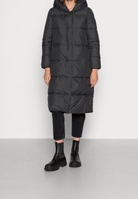 Svart puffjacka med huva, med en quiltad design och långa ärmar, i kombination med mörka cropped byxor och kraftiga svarta ankelboots.