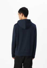 Marinefarbener Kapuzenpullover mit langen Ärmeln, aus weichem Stoff, entspannter Schnitt und gerippten Bündchen. Im minimalistischem Design ohne sichtbare Logos gestaltet.