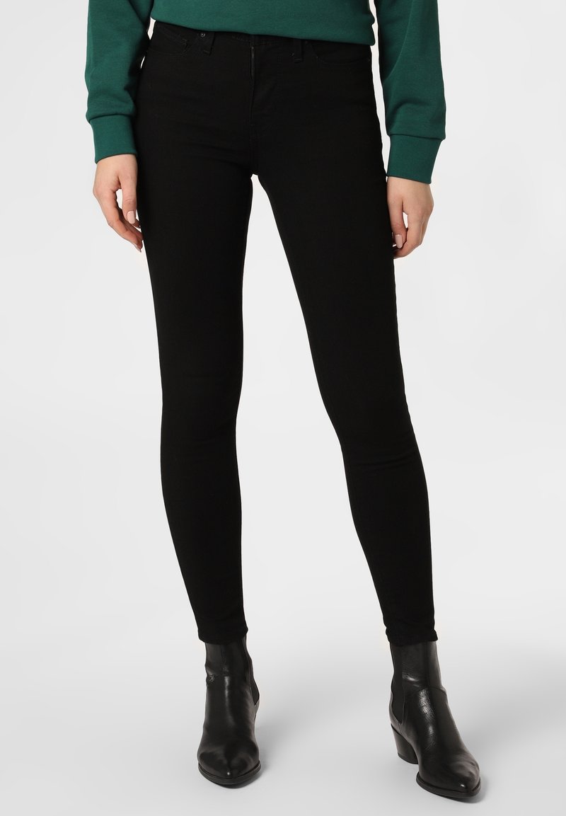 Black skinny jeans with a smooth texture, high-rise waist, and five-pocket design. Paired with black ankle boots.
