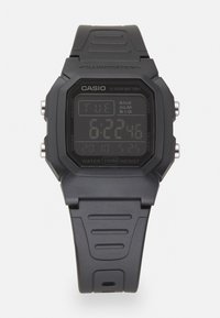 Montre numérique avec un boîtier rectangulaire en plastique noir, écran LCD affichant l'heure, la date et l'alarme, et un bracelet en caoutchouc noir texturé. Résistante à l'eau jusqu'à 100 m.