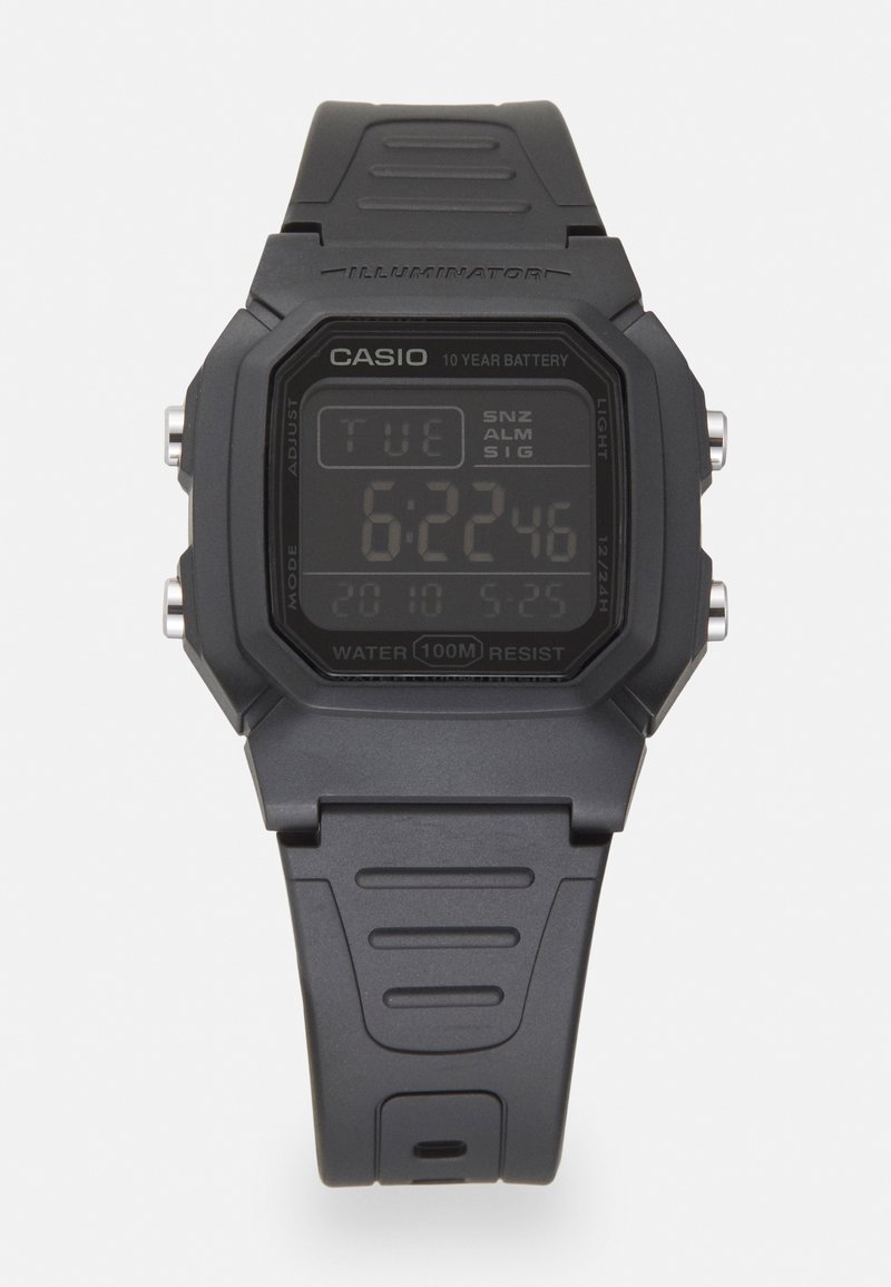 Montre numérique avec un boîtier rectangulaire en plastique noir, écran LCD affichant l'heure, la date et l'alarme, et un bracelet en caoutchouc noir texturé. Résistante à l'eau jusqu'à 100 m.