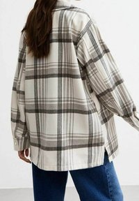 Camicia a quadri in beige e grigio, realizzata in tessuto testurizzato. Presenta una vestibilità rilassata, maniche lunghe, polsini con bottone e spacco laterale.