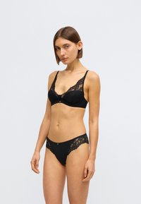 Melnā mežģīņu un auduma krūšturis ar V veida izgriezumu, regulējamām lencēm un dekoratīviem mežģīņu akcentiem. Saskaņotas melnas biksītes ar mežģīņu apdari.