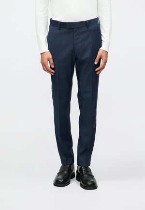 Marineblå skræddersyede bukser med en glat tekstur, der har en lige pasform og kant langs forsiden. Båret med sorte slip-on sko.