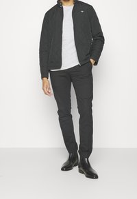 Black quilted jacket with a high collar, worn over a light gray shirt, paired with black slim-fit pants and black chelsea boots.