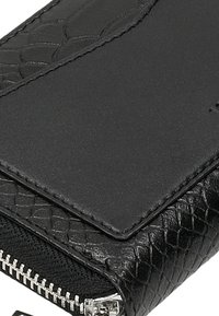 Černá texturovaná peněženka s hladkou horní částí a embosovaným vzorem. Obsahuje stříbrný zip pro uzavření a látkovou podšívku.
