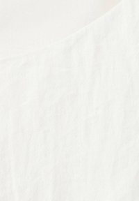 Gros plan sur un tissu blanc avec un bord subtilement plié et une surface douce, légèrement texturée.
