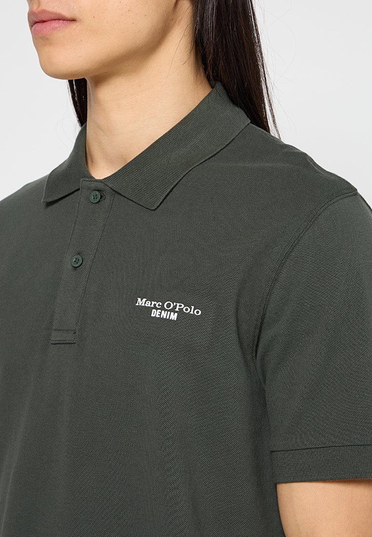 Dunkelgrünes Polohemd aus strukturiertem Stoff, mit spitzem Kragen und kurzen Ärmeln. Zeigt "Marc O'Polo DENIM" in Weiß.