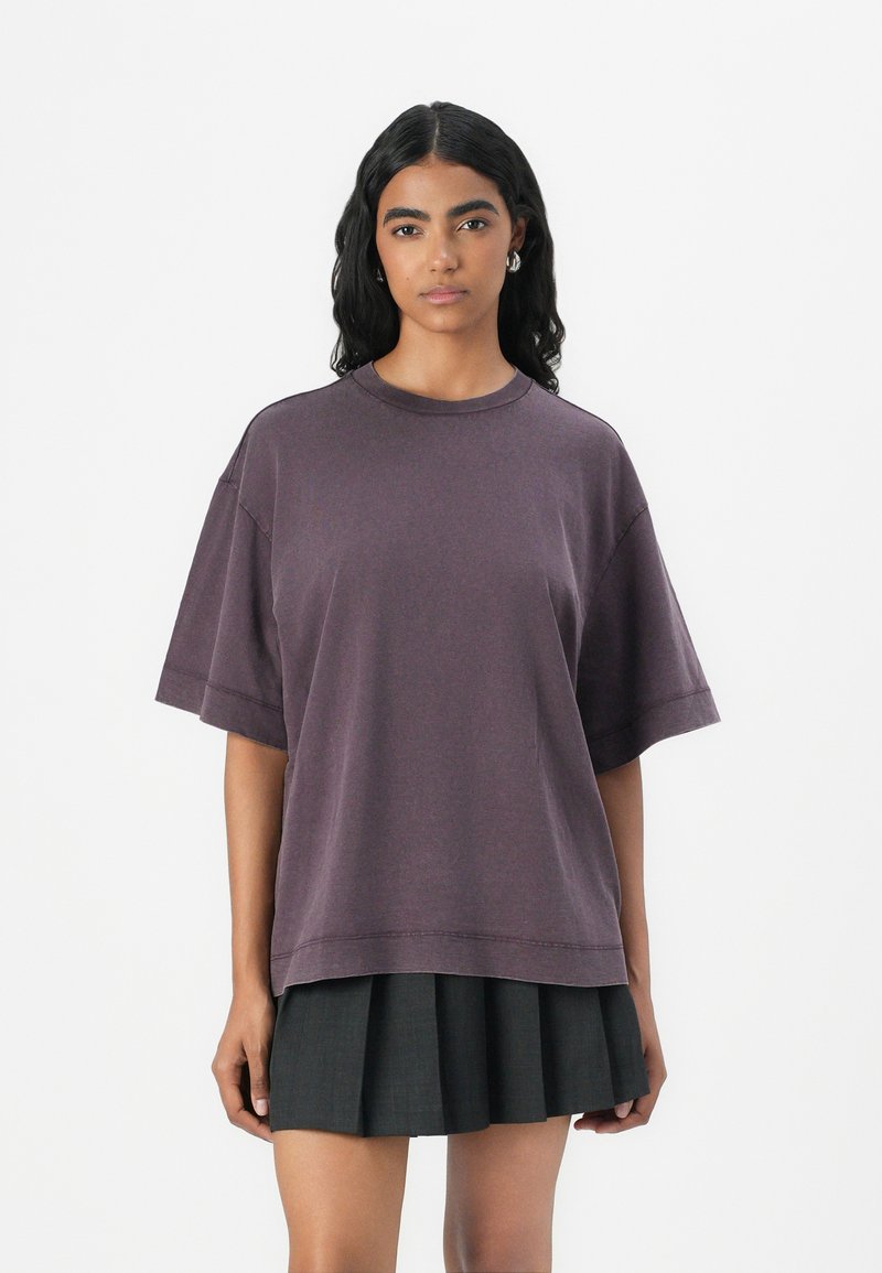 T-shirt viola oversize realizzato in tessuto morbido con scollo rotondo e maniche corte, abbinato a una gonna nera plissettata.