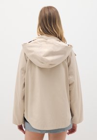 Beige leichte Jacke mit Kapuze, mit lockerer Passform, langen Ärmeln und glatter Textur. Keine sichtbaren Muster oder Beschläge.