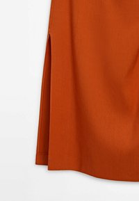 Jupe en tissu orange rouille avec une fente latérale et des coutures visibles sur fond blanc.