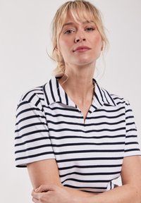 Katoenen gestreepte polo shirt in wit en marineblauw. Kenmerken zijn een kraag, korte mouwen en een ribbelstructuur. Accentueren door gelijke horizontale strepen.