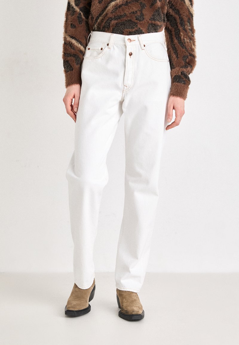 Jeans en denim blanco con cintura alta, piernas rectas y costuras en contraste. Combinados con un suéter marrón texturizado de patrón y botas de tobillo marrones.