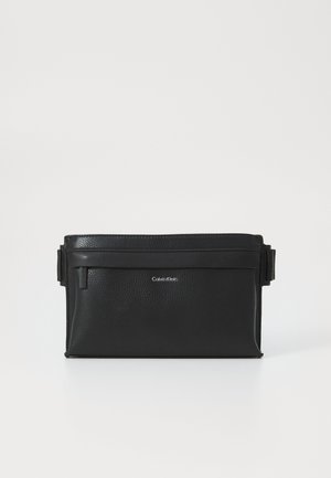 Sac banane en cuir noir Calvin Klein avec poche avant zippée et sangles latérales réglables sur fond blanc.