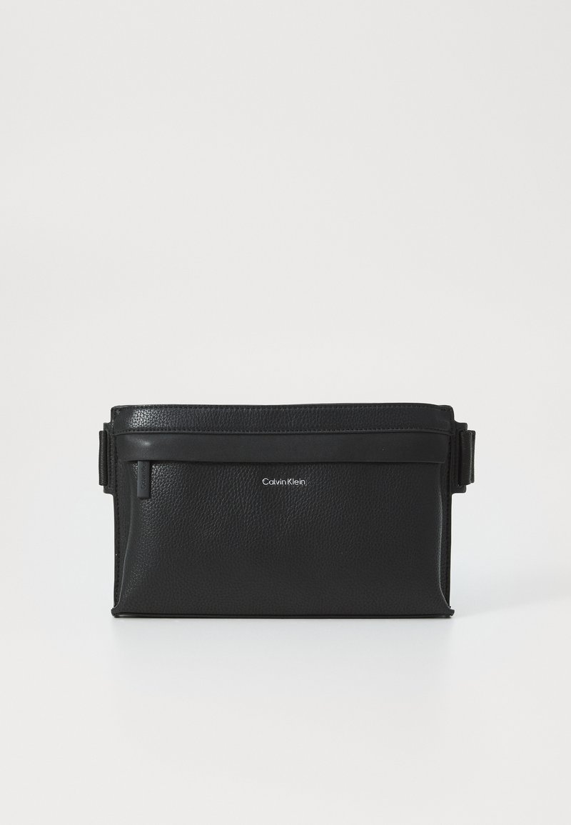 Sac banane en cuir noir Calvin Klein avec poche avant zippée et sangles latérales réglables sur fond blanc.