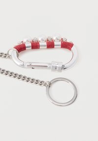 Hõbedast metallist karabiin punase kangasümbrise ja dekoratiivsete pärlitega. Sisaldab hõbedast ketti ja ümmargust võtmerõngast.