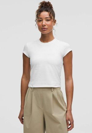 T-shirt bianca aderente a maniche corte con scollo rotondo, realizzata in tessuto liscio, abbinata a pantaloni beige a vita alta. Design semplice.