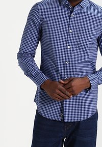 Marinblå och vit rutigt skjorta med knäppning, långa ärmar och bröstficka, tillverkad av lättviktsmaterial.