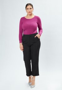 Top de manga larga fucsia con cuello redondo, combinado con pantalones negros de cintura alta. La modelo lleva puestos unos zapatos de tacón plateados y brillantes.