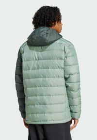 Chaqueta acolchada con un diseño bicolor: cuerpo verde claro y capucha verde oscura. Tela texturizada y líneas de acolchado horizontales.