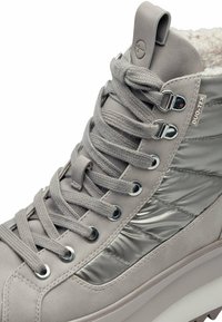 Baskets montantes grises en cuir synthétique avec des accents brillants, présentant un col texturé, des œillets en métal et une épaisse semelle blanche.