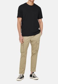 Sort bomulds T-shirt parret med beige cargo bukser med to sidelommer og en tætsiddende pasform, afsluttet med sorte og hvide sneakers.