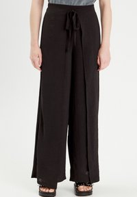 Pantalon large noir en tissu texturé avec une taille à nouer. Présente une coupe décontractée et un design légèrement évasé, adapté à diverses occasions.