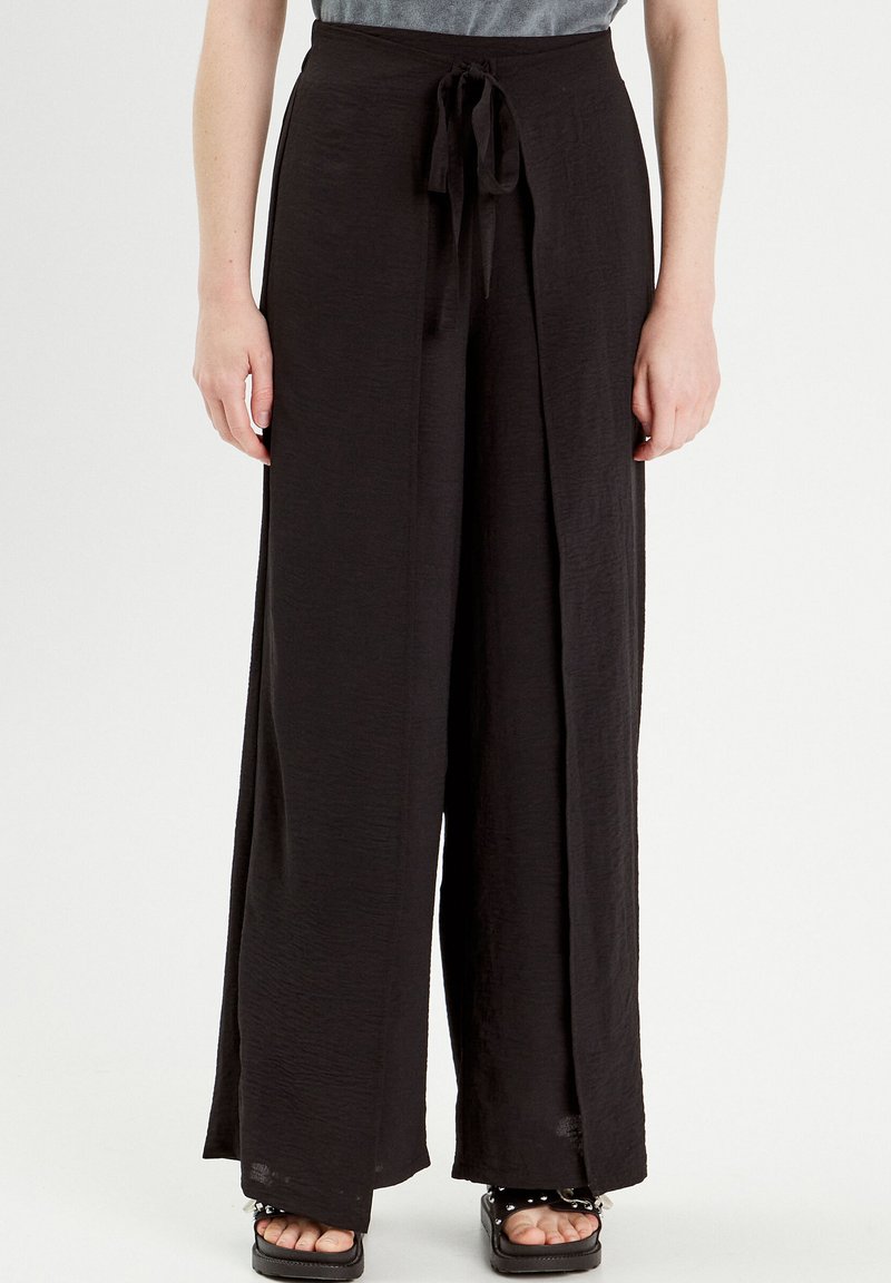 Pantalon large noir en tissu texturé avec une taille à nouer. Présente une coupe décontractée et un design légèrement évasé, adapté à diverses occasions.