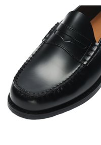 Μαύρο γυαλιστερό δερμάτινο μοκασίνι με ραφή μοκ μύτης και λεπτομέρεια με λωρίδα πένι, κοντινή λήψη από μπροστά και πλάγια όψη.