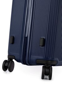 Námorní kufr s tvrdou skořepinou, který má vertikální žebrovanou texturu, hladký zip a čtyři černá kolečka pro snadnou manipulaci. Kompaktní design z odolného materiálu.